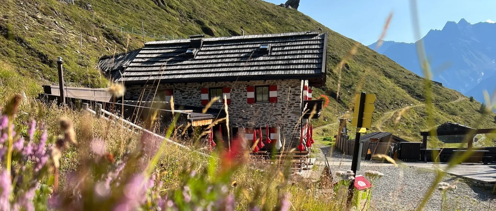 Steinhütte mit roten Fensterläden in Alpenlandschaft